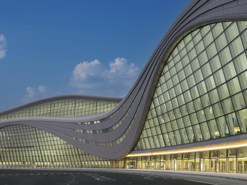 The exterior of Zayed International Airport, a glass front airport terminal against a blue evening sky