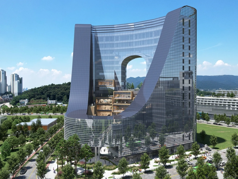 Modern curved glass building with a large central arch, surrounded by greenary and nearby city buildings.