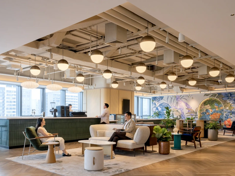 Modern office lounge with a coffee bar, seating area, warm lighting, wooden floors and colourful walls.