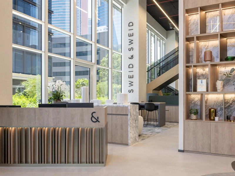 Interior of a warm, light-filled modern office with a shelf of objects and an orchid on the reception desk