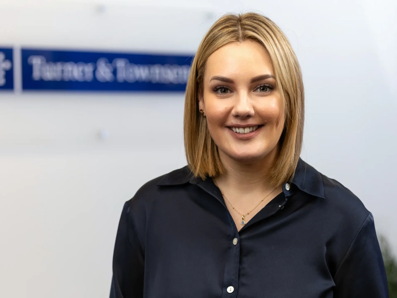 Portrait of Steph Marahall, Managing Director, UK Cost Management, standing in office in front of Turner & Townsend sign