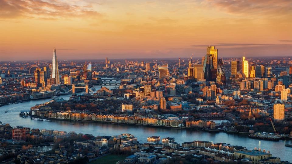 Panoramic, elevated view of the urban London skyline with soft, golden sunlight during sunrise, England