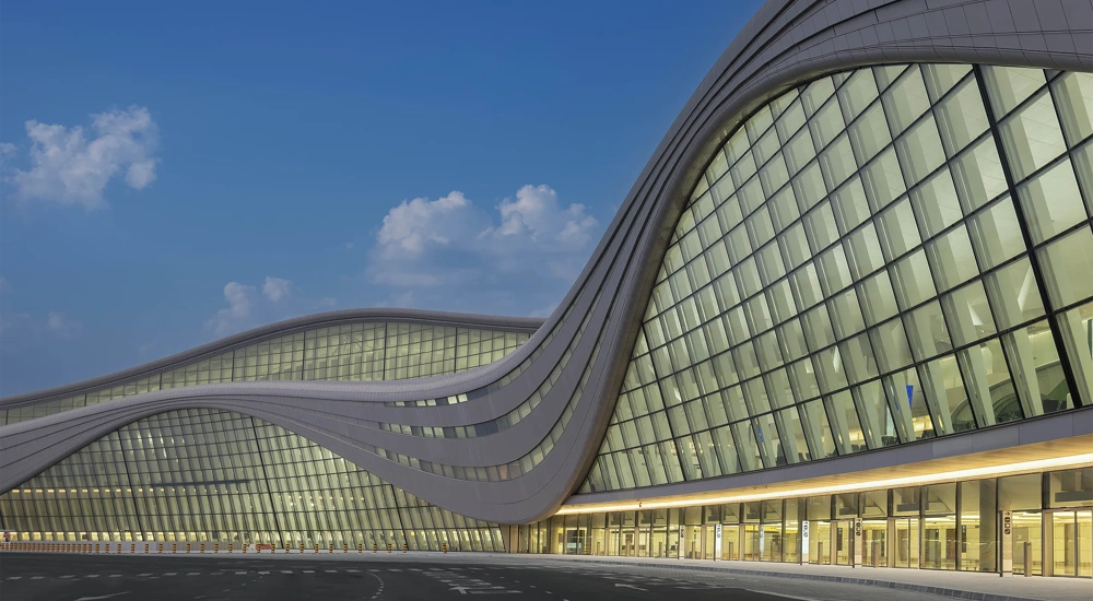 The exterior of Zayed International Airport, a glass front airport terminal against a blue evening sky