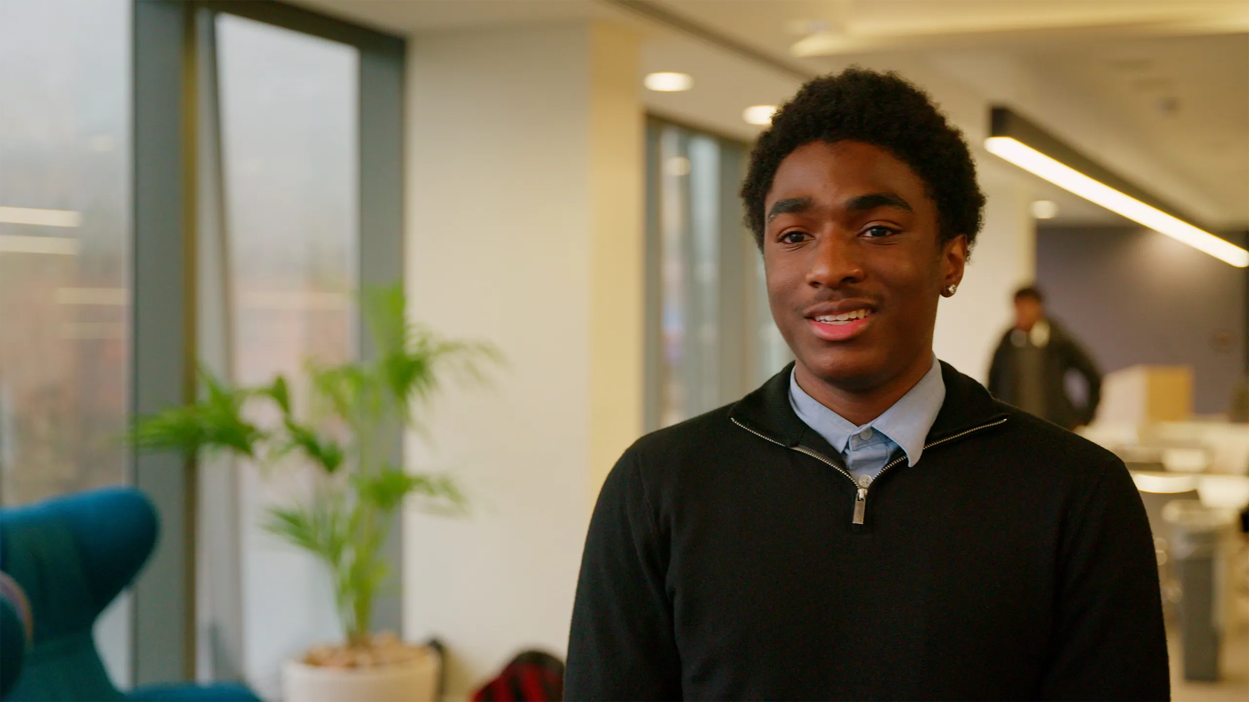 Image of young male, standing in plant based office, smiling.
