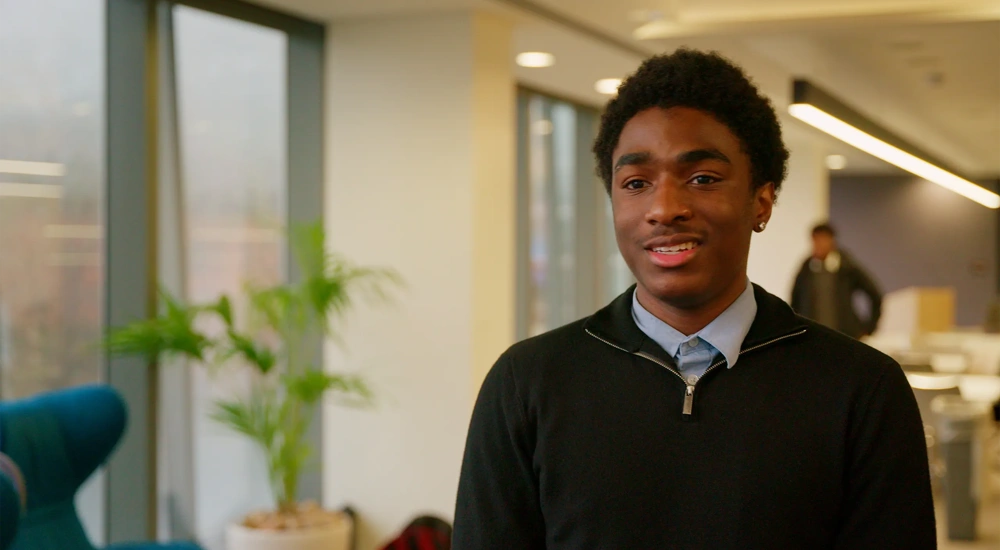 Image of young male, standing in plant based office, smiling.