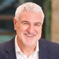 Steve Perkins, Director, outside in front of a blurred brown background featuring a building and mix of natural and urban elements.