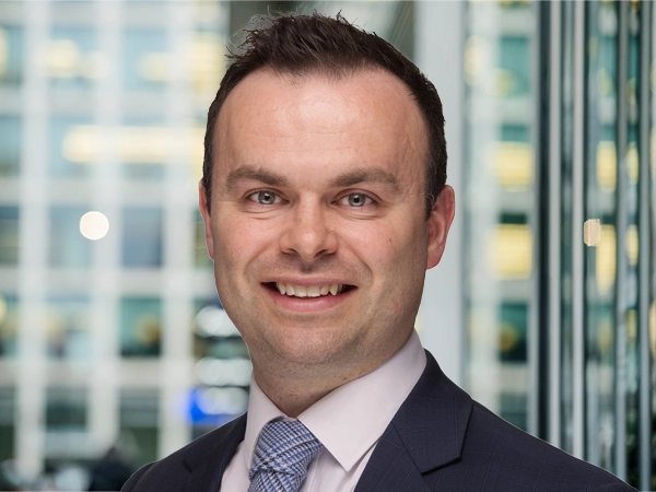 Portrait of Chris Swann, Associate Director, Advisory and Consulting, with city landscape featuring building with lots of windows in the background.