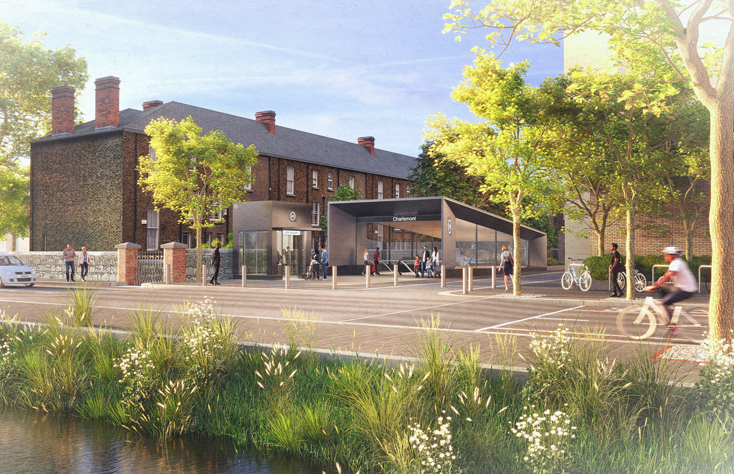 The entrance to a modern metro station, next to brickwork buildings and with a background of trees. 