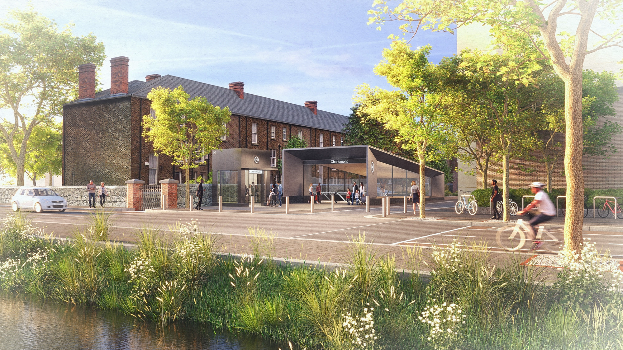 The entrance to a modern metro station, next to brickwork buildings and with a background of trees.