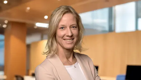 Portrait of Bettina Würfel, Managing Director, standing in an office with warm wooden backdrop and windows