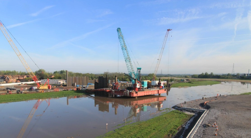 Barge with cranes working on a river flood barrier construction site in the UK