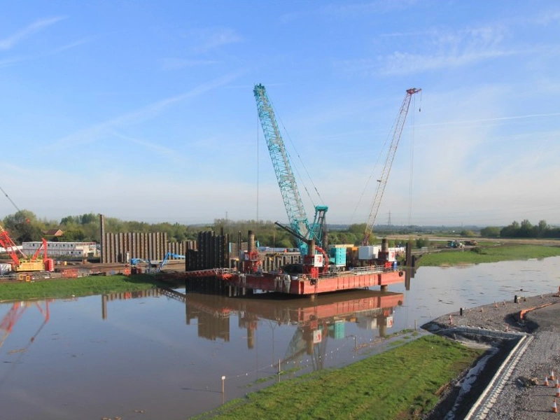Barge with cranes working on a river flood barrier construction site in the UK