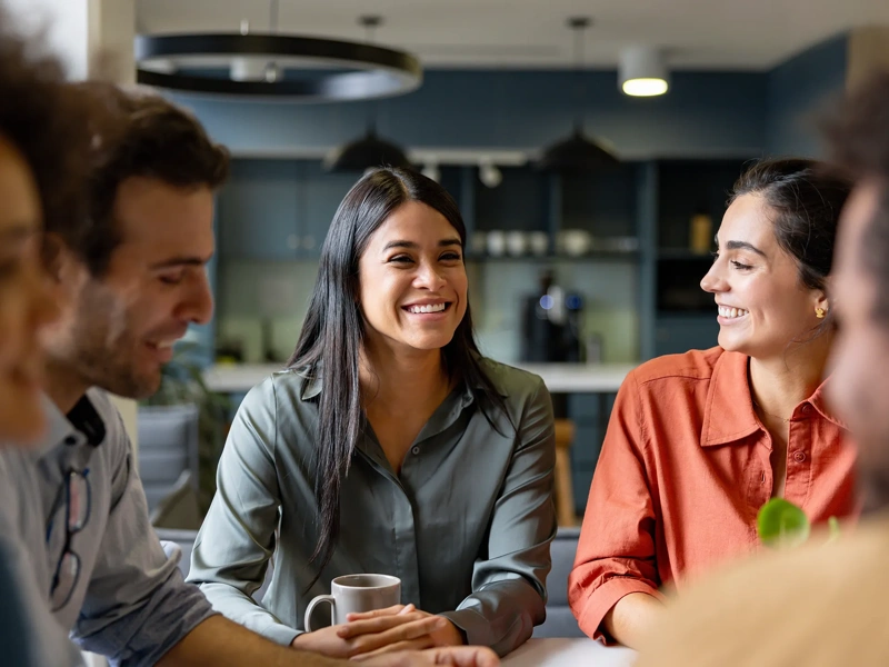 Group of colleagues sitting together having a conversation, gathered around a table with coffee mugs.