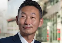 Portrait of Hisanao Kajiura, Managing Director, Japan, standing outside in front of buildings featuring an urban cityscape with a mix of architectural styles. The scene includes some windows and red features, adding a touch of color.