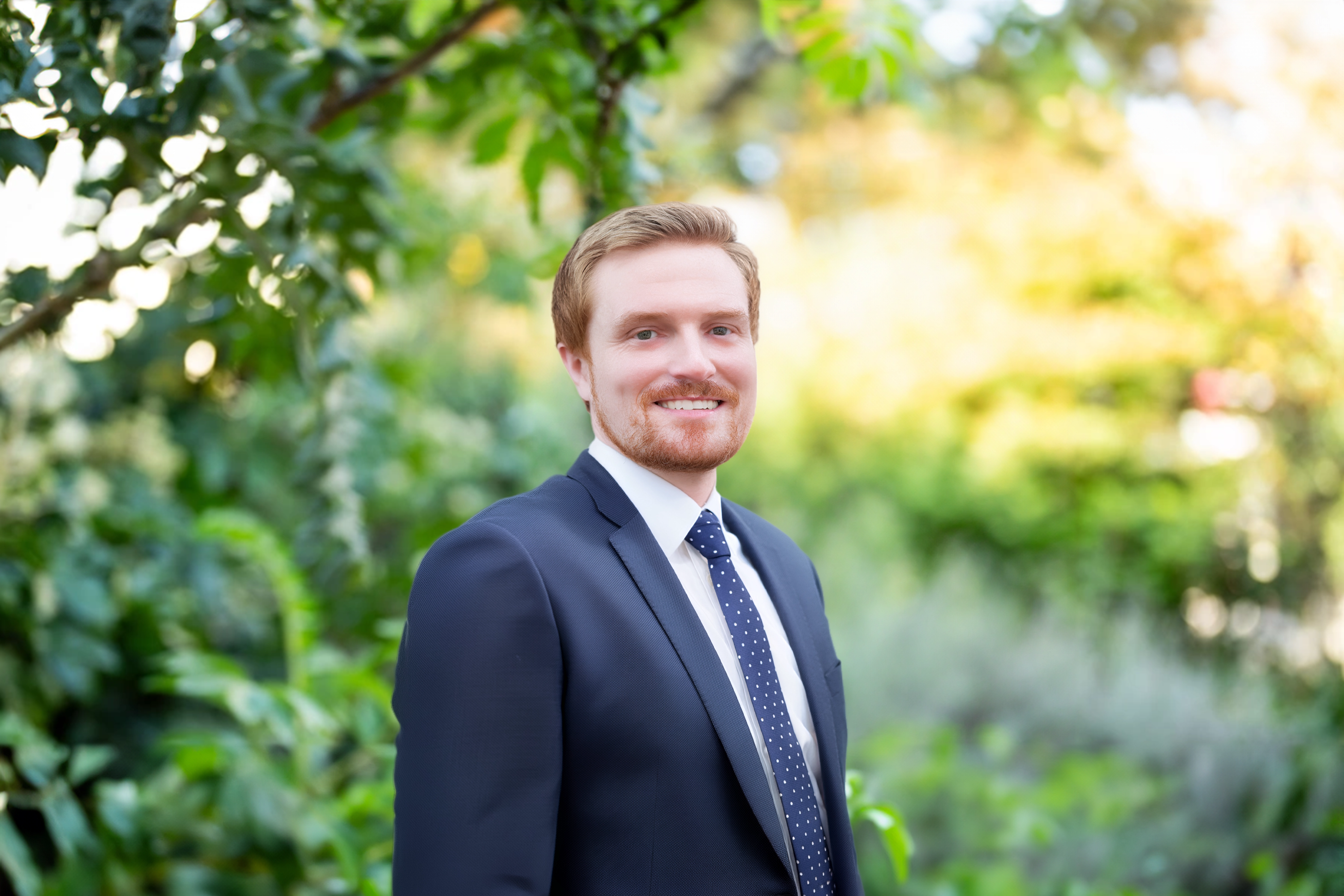 Portrait of Joe Connolly, Industrial and Logistics Lead, North America, Standing outside infront of green plants smiling.