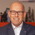 Portrait of Philip Matthews, Managing Director, Ireland, outside in front of a blurred brown background featuring a building and mix of natural and urban elements.