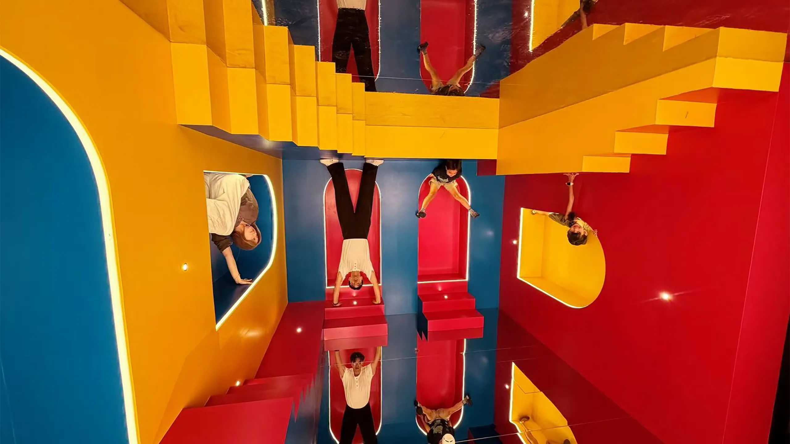 Colourful mirrored installation with red, blue and yellow geometric structures and people reflected throughout.