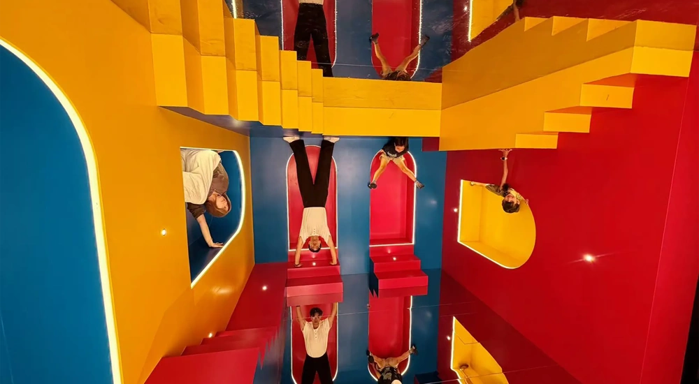 Colourful mirrored installation with red, blue and yellow geometric structures and people reflected throughout.