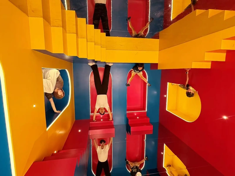 Colourful mirrored installation with red, blue and yellow geometric structures and people reflected throughout.
