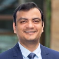 Portrait of Ashish Jain, Country Manager, outside in front of a blurred brown background featuring a building and mix of natural and urban elements.