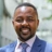 Robert Gichohi, Country Director, standing outside in front of an outdoor urban setting, featuring modern architectural elements with clean lines. There are hints of greenery, suggesting some trees or plants.