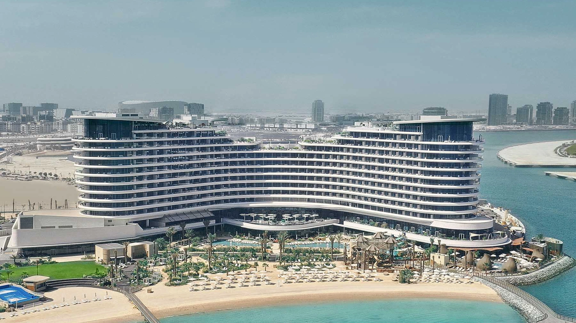 A beach front multi-story hotel resort complex with sun loungers and the sea in the foreground.