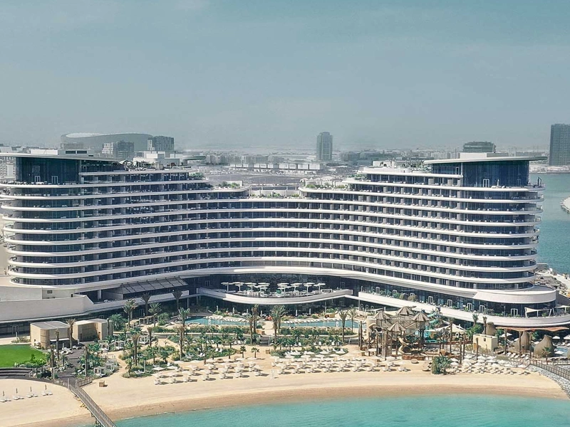 A beach front multi-story hotel resort complex with sun loungers and the sea in the foreground.