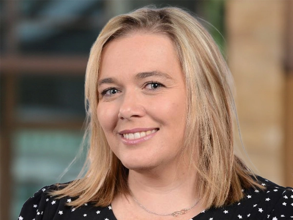 Wendy Cerutti, Head of Cost Management, Johannesburg, outside in front of a blurred brown background featuring a building and mix of natural and urban elements.