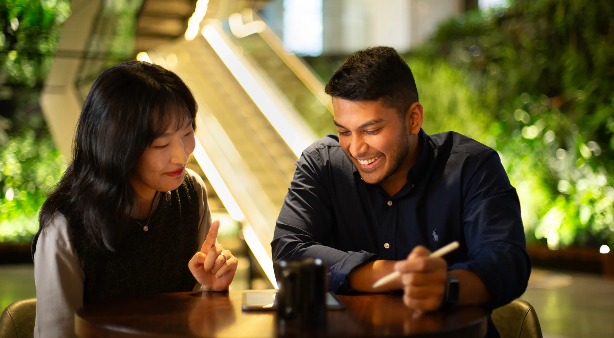 Two colleagues sitting together looking at a tablet in a plant-filled office.