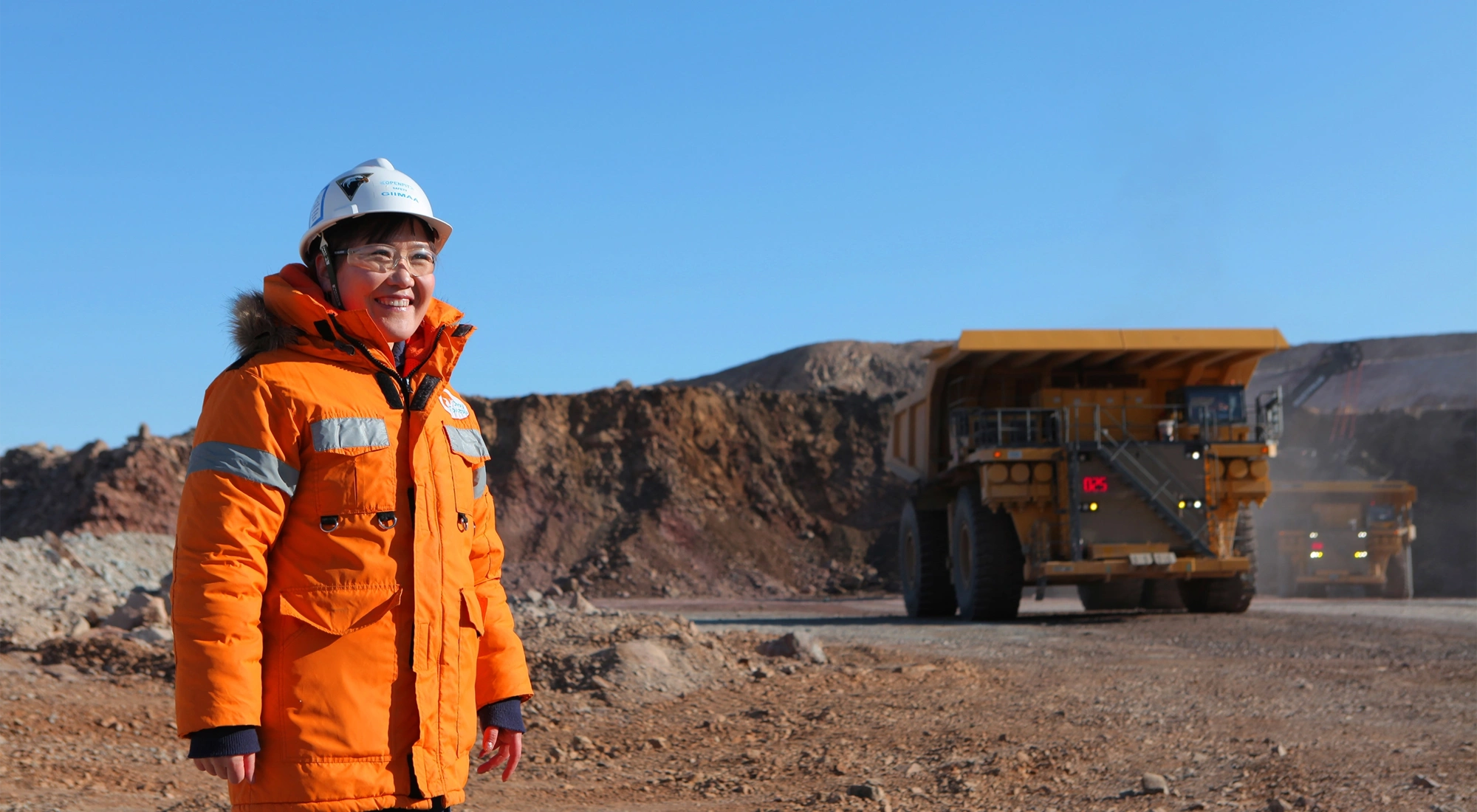 Woman in bright orange construction site uniform standing in a sandy landscape