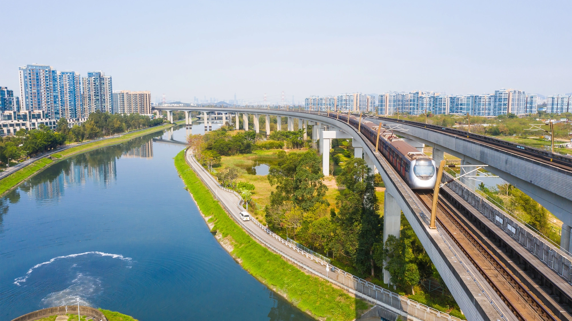 Picture of train going over water stream and fields with city in the background.