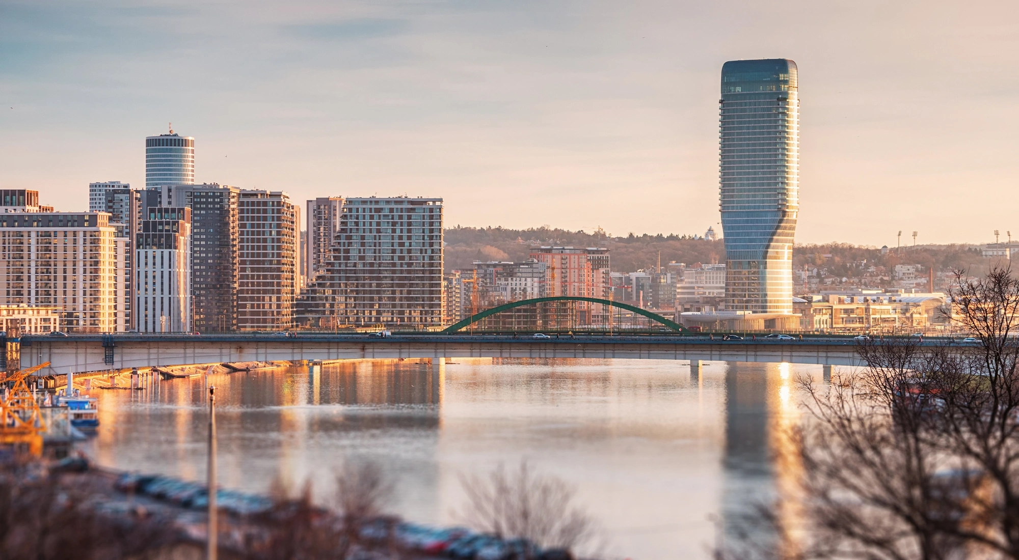 City skyline with modern high rise buildings and a bridge over a river at sunset.