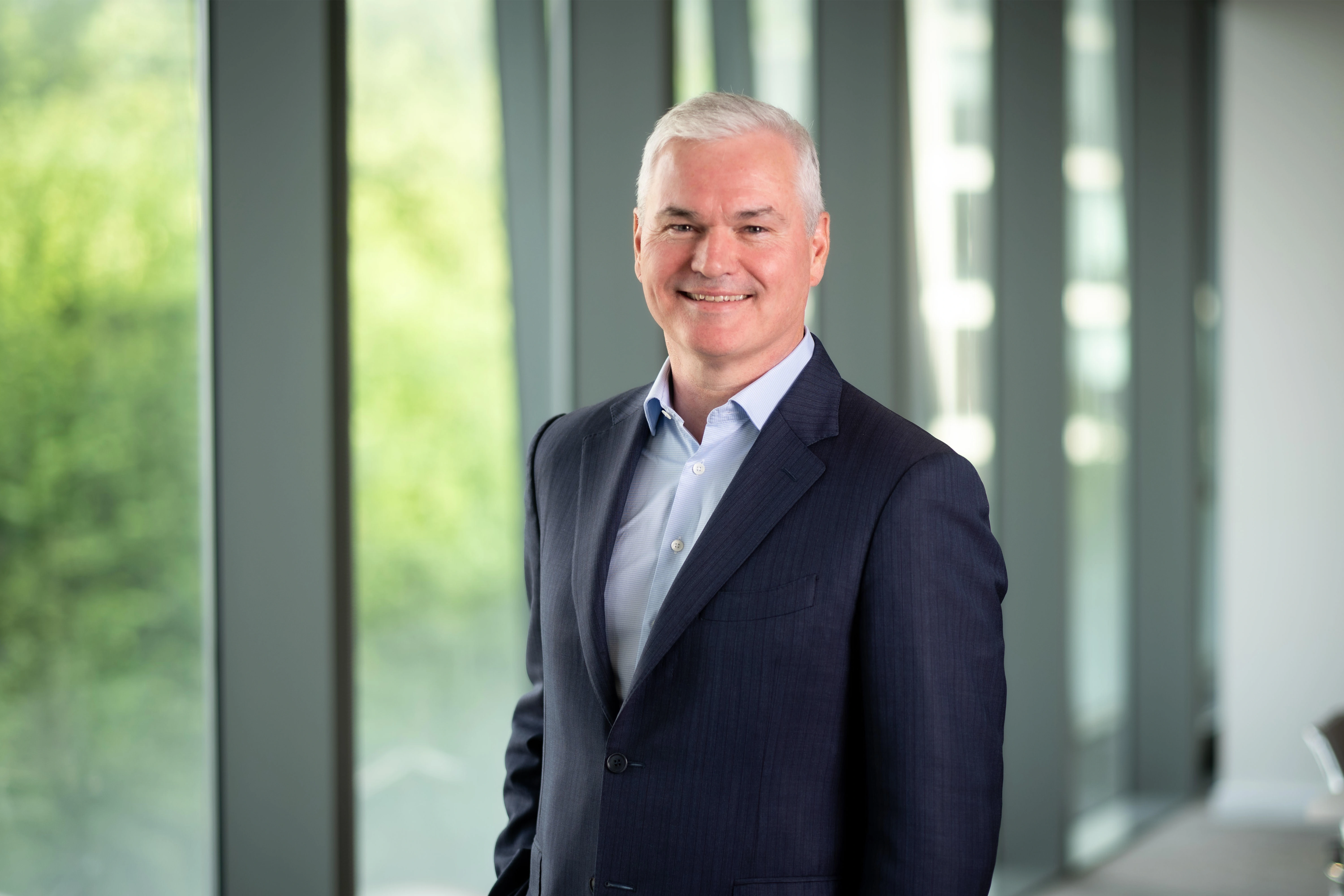 Vincent Clancy, CEO, smiling in front of a window with trees behind him