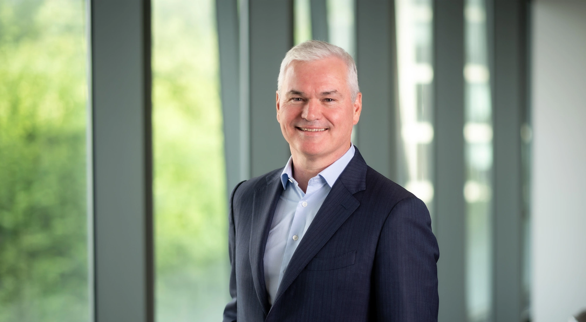 Vincent Clancy, CEO, smiling in front of a window with trees behind him