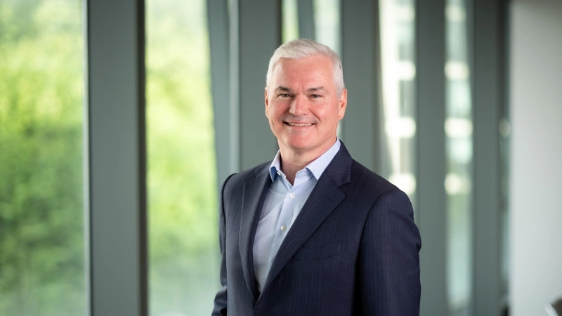 Vincent Clancy, CEO, smiling in front of a window with trees behind him