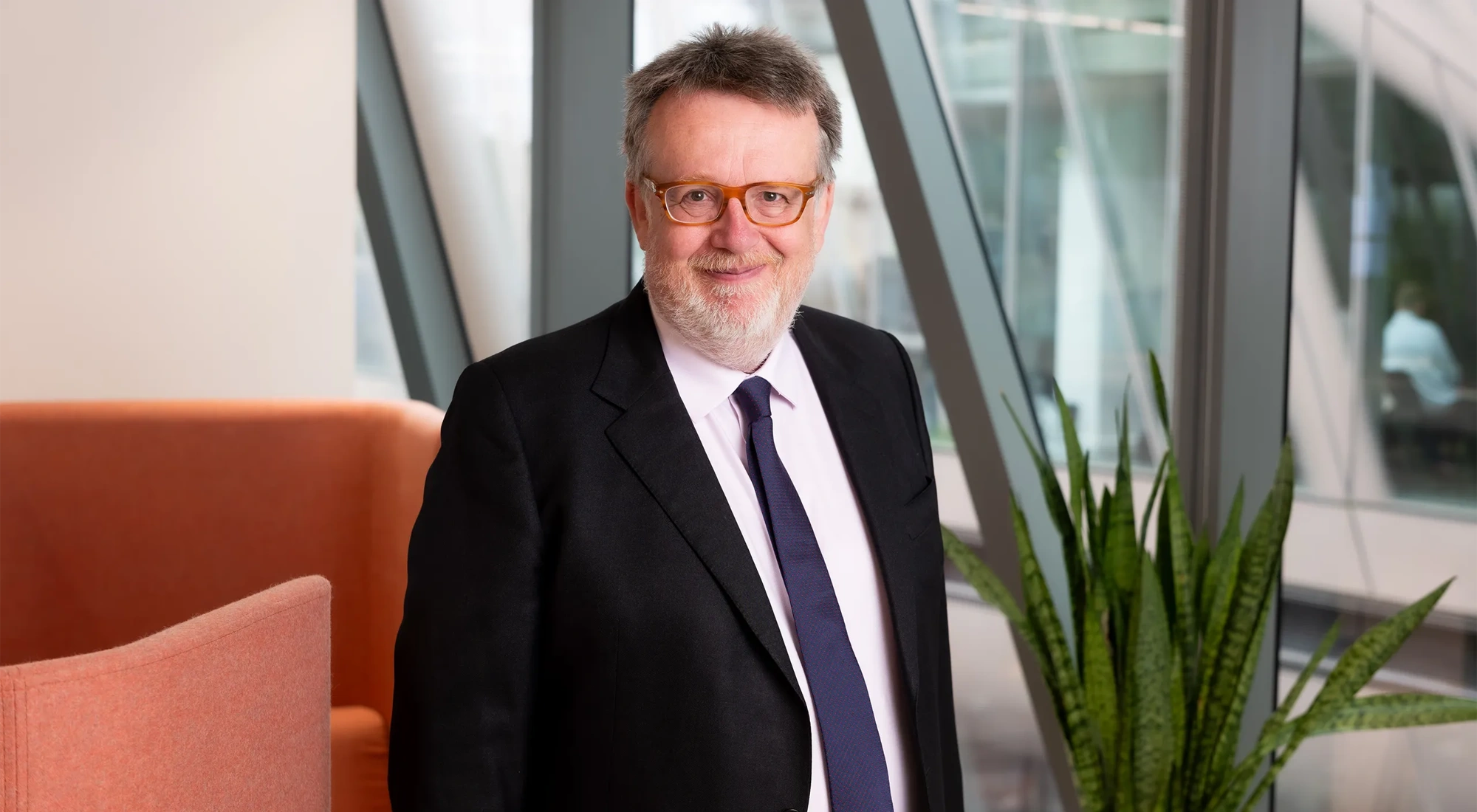 Portrait of Chris Hillier, Projects Expert, UK, standing in office space against orange chair.