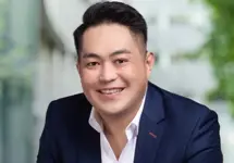 Portrait of Terence Koh, Project Director, standing outside in front of an outdoor urban setting, featuring modern architectural elements with clean lines. 