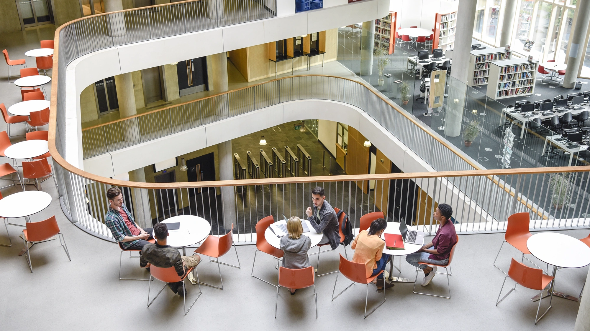 Furniture in open plan building with modern staircase and college students meeting friends.