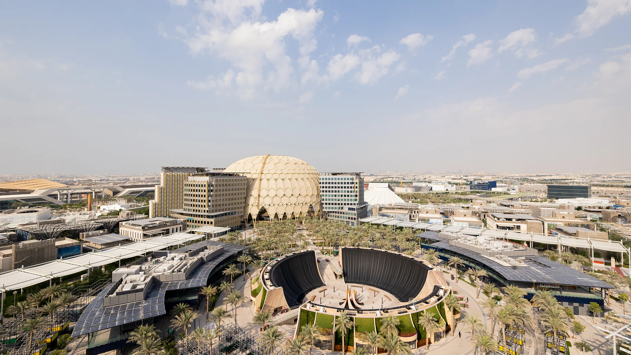 Ariel view of Dubai Expo, modern city complex with large building, curved structures and surrounding roads under a clear sky