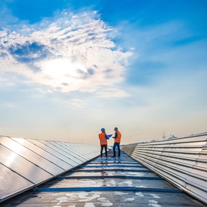 Two men in safety vests next to solar panels 
