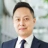 Daniel Cheung, Strategic Lead, Hong Kong & Macau, and Head of Infrastructure, Northeast Asia, standing outside in front of an outdoor urban setting, featuring modern architectural elements with clean lines. There are hints of greenery, suggesting some trees or plants.