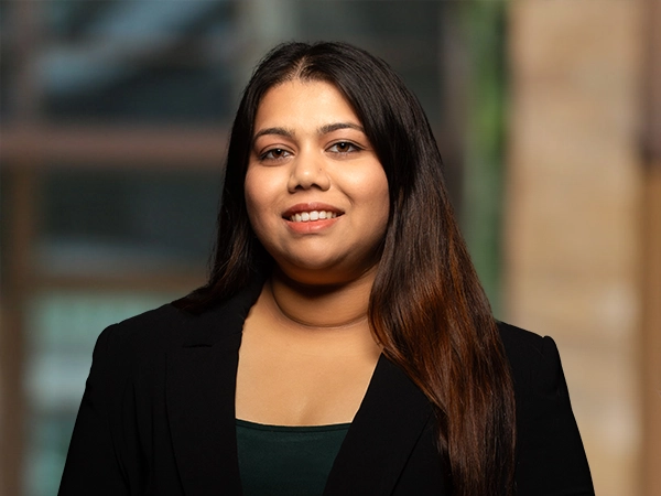Portrait of Dionne Pereira, Senior Sustainability Consultant, outside in front of a blurred brown background featuring a building and mix of natural and urban elements.