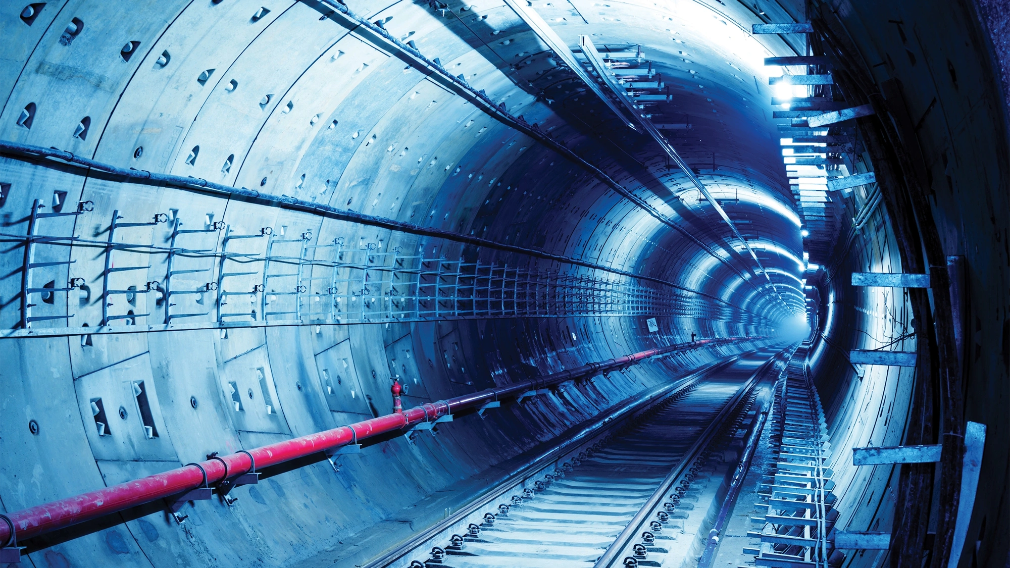 Underground transit tunnel with railway tracks illuminated by blue light