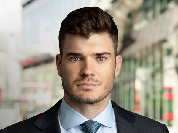 Portrait of Christian Weitz, Senior Project Manager, standing outside in front of buildings featuring an urban cityscape with a mix of architectural styles. The scene includes some windows and red features, adding a touch of color.