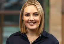 Portrait of Stephanie Marshall, Managing Director, UK Real Estate Cost Management, outside in front of a blurred brown background featuring a building and mix of natural and urban elements.