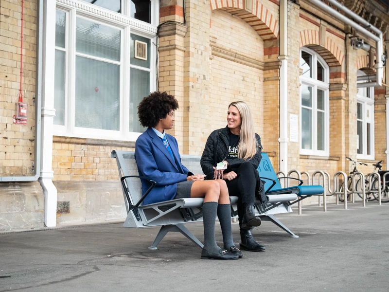 Child in school uniform sitting next to woman in train station platform chatting