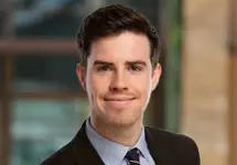  Portrait of Louis Hemming, Associate Director, UK, Life Sciences, outside in front of a blurred brown background featuring a building and mix of natural and urban elements.