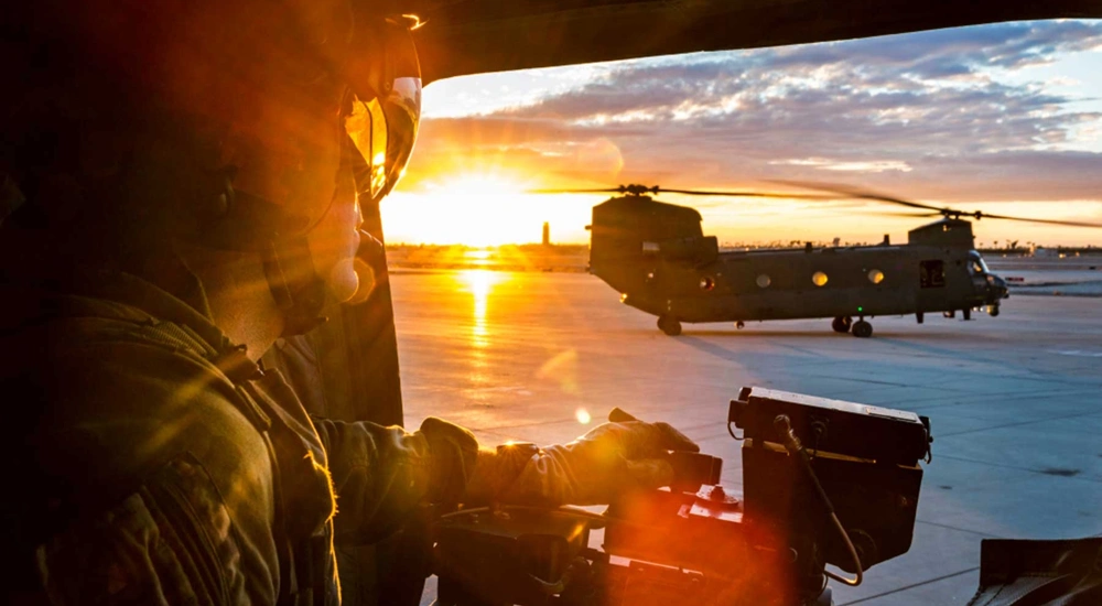 RAF operator looking out of helicopter toward surrounding airfield at sunsent