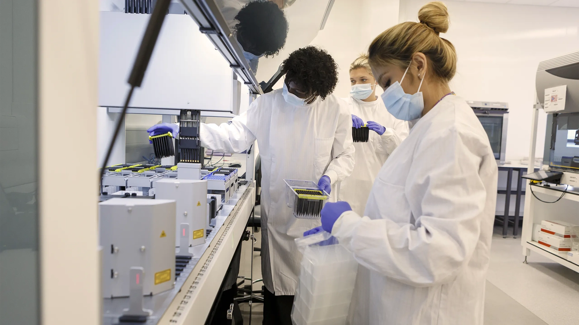 Students in a university science lab with white coats and face masks on working on machine.