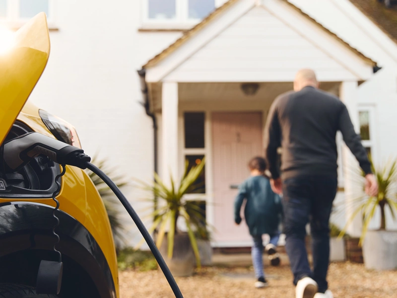 Yellow car being charged in driveway while a man and boy enter the house